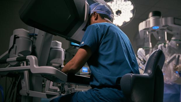 Surgeon in scrubs looks into viewport of large Da Vinci robotic surgeon.