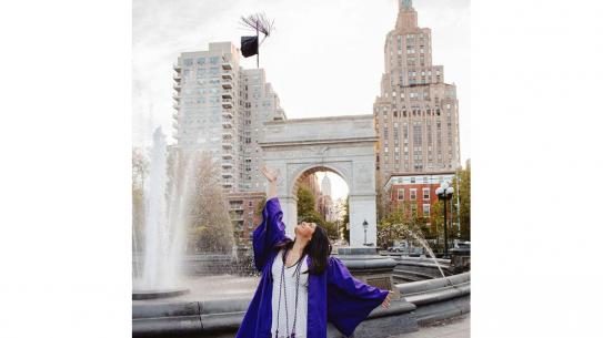 female graduate tossing cap in air in front of washington square arch