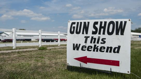 Awhite sign that says "Gun show this weekend" with a red arrow pointing to the left