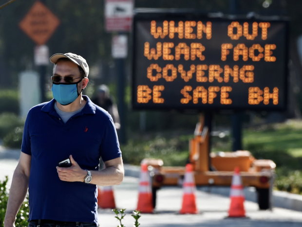 man wearing a face mask in front of sign "when out wear face covering be safe"