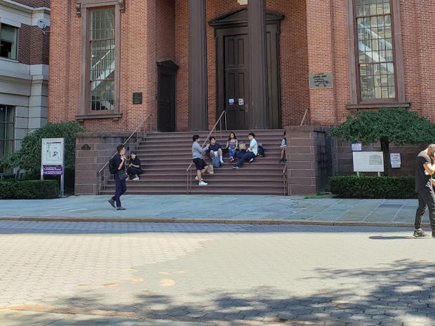 students sitting on steps of brick building with columns