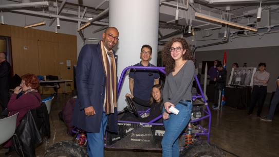 Students in NYU Tandon's Motorsports team display their vehicle to an alumnus