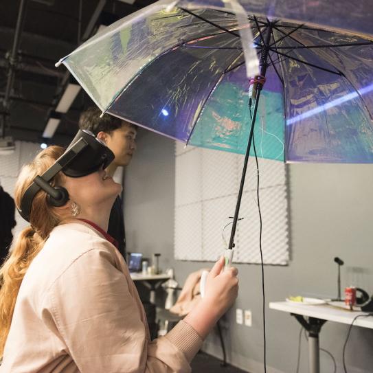 student wearing VR headset looking up at umbrella student wearing VR headset looking up at umbrella