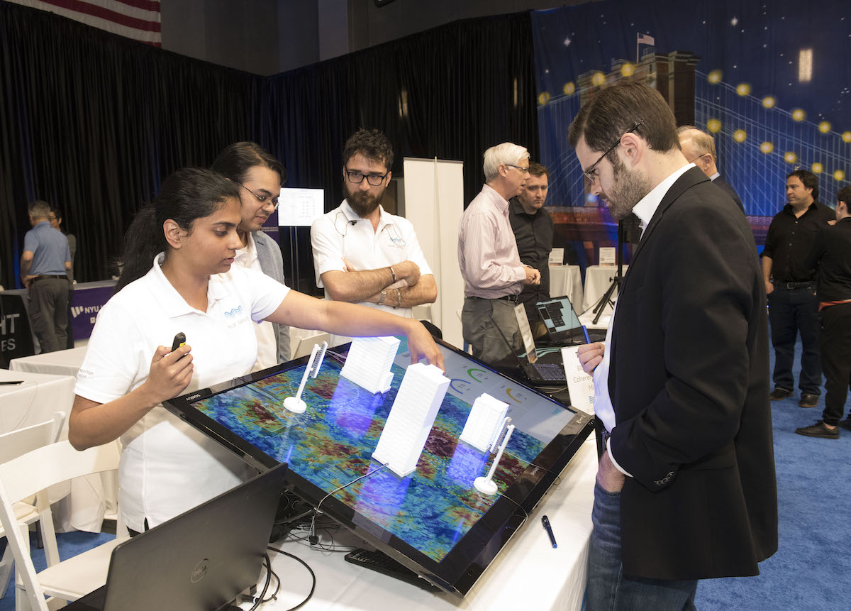 female student points at model of urban wireless towers as man in blazer watches